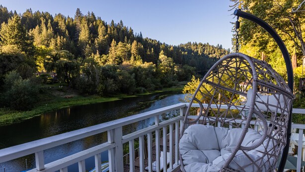 A wooden deck with a white railing overlooking a river, surrounded by dense forest.