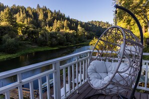 A wooden deck with a white railing overlooking a river, surrounded by dense forest.