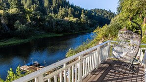 A wooden deck with a white railing overlooking a river, surrounded by trees.