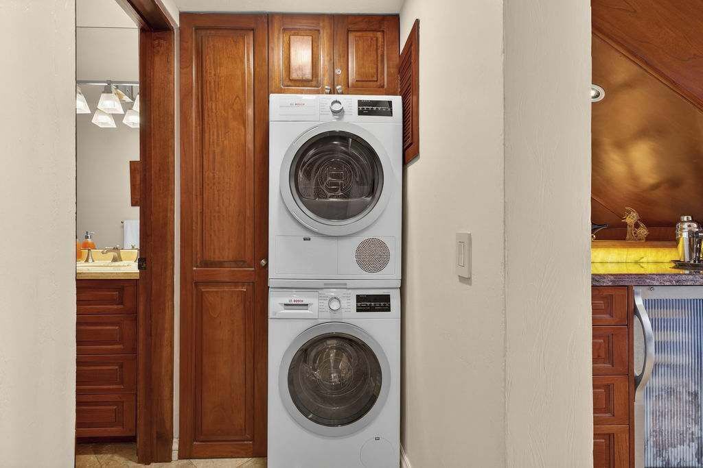 A laundry area with stacked washing machines, wooden cabinets, and a sink.
