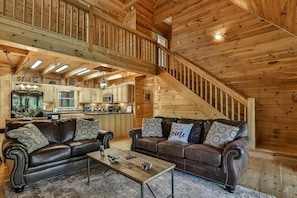 A spacious living room with two leather sofas, a coffee table, and a staircase leading to an upper level.