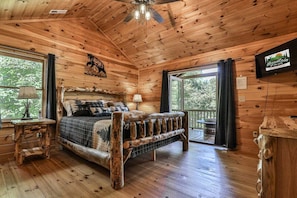 A log cabin bedroom with a wooden bed, a ceiling fan, and a television mounted on the wall.