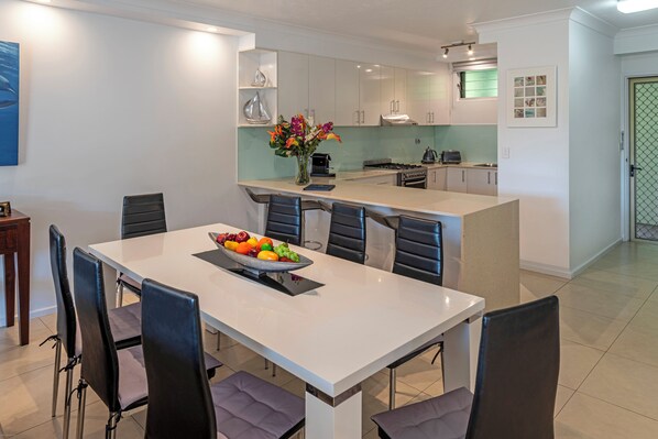 Una cocina moderna con una isla central, armarios blancos y un comedor con mesa preparada para cuatro.