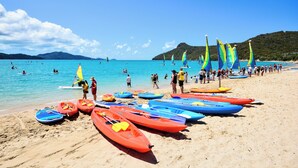 Una playa con varias kayaks y canoas alineadas sobre la arena, un cielo azul despejado y un mar tranquilo.