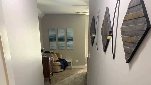 A hallway with a carpeted floor, a beige couch, and three wall-mounted light fixtures. - Bettendorf Condo: Fireplace, King Bed & Family Fun! (Bettendorf)