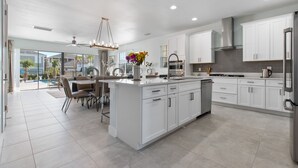 A modern kitchen with white cabinetry, a central island, and a dining area with a ceiling fan.