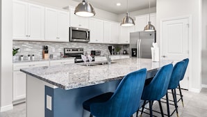 A modern kitchen with white cabinets, a granite countertop, stainless steel appliances, and blue bar stools.