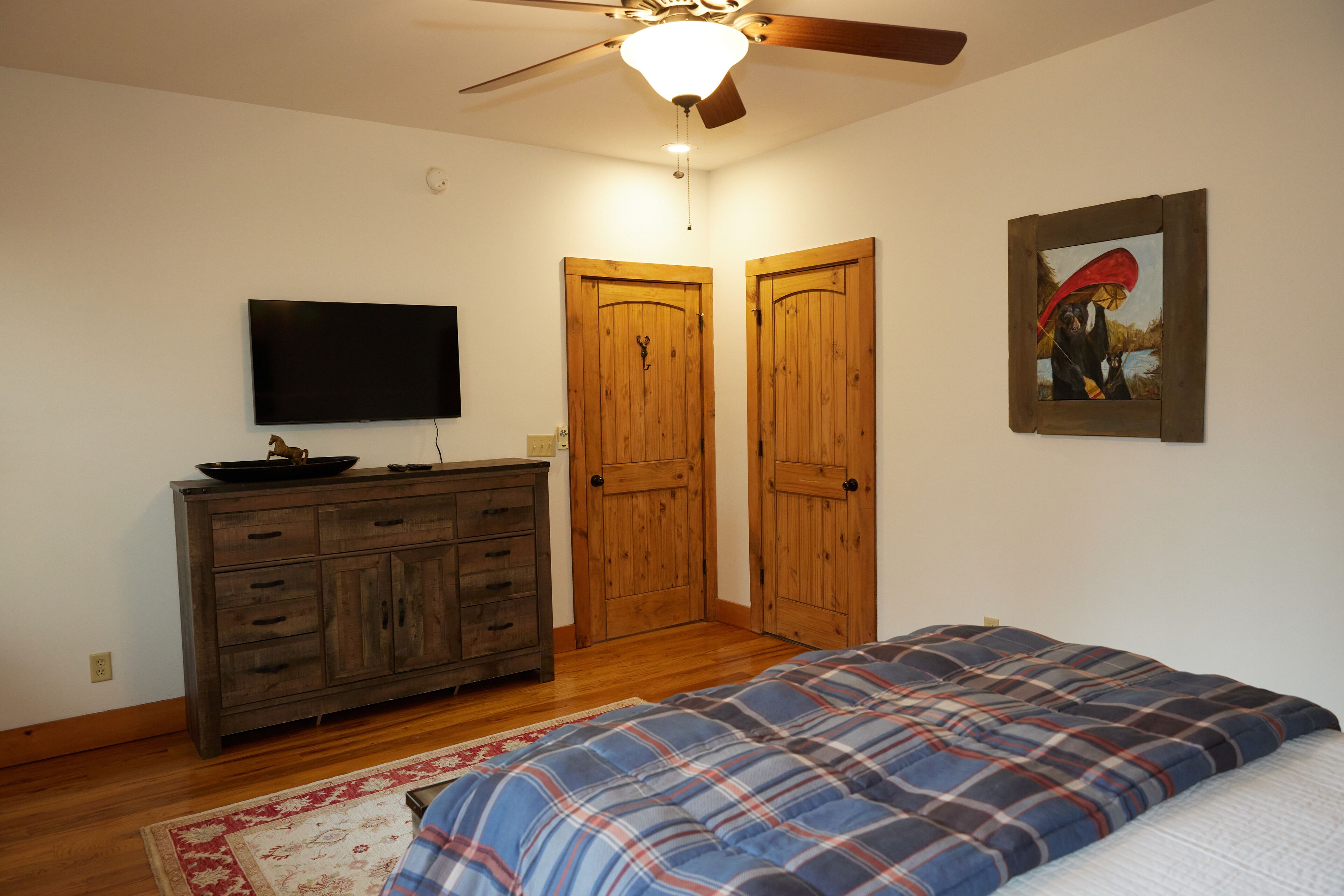 A bedroom with a bed, wooden dresser, television, and a ceiling fan.
