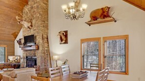 Ein geräumiges Wohnzimmer mit hohen Decken, einem Kamin aus Stein und einem Essbereich mit Holzmöbeln.
