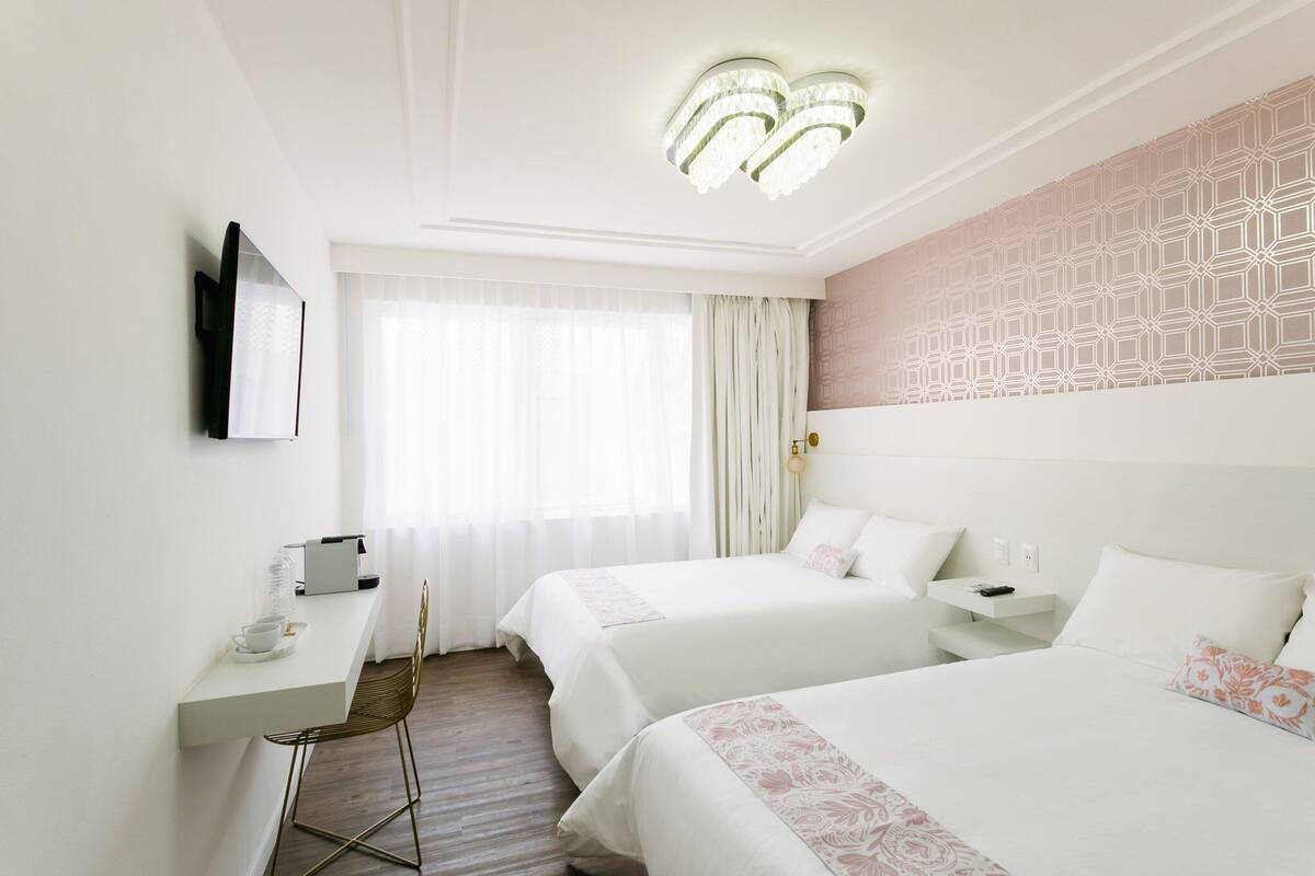 Hotellihuone, jossa on kaksi sänkyä, työpöytä, tuoli, seinälle asennettu televisio ja kuviollinen seinä.