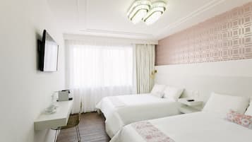 A hotel room with two beds, a desk, a chair, a TV mounted on the wall, and a patterned wall.