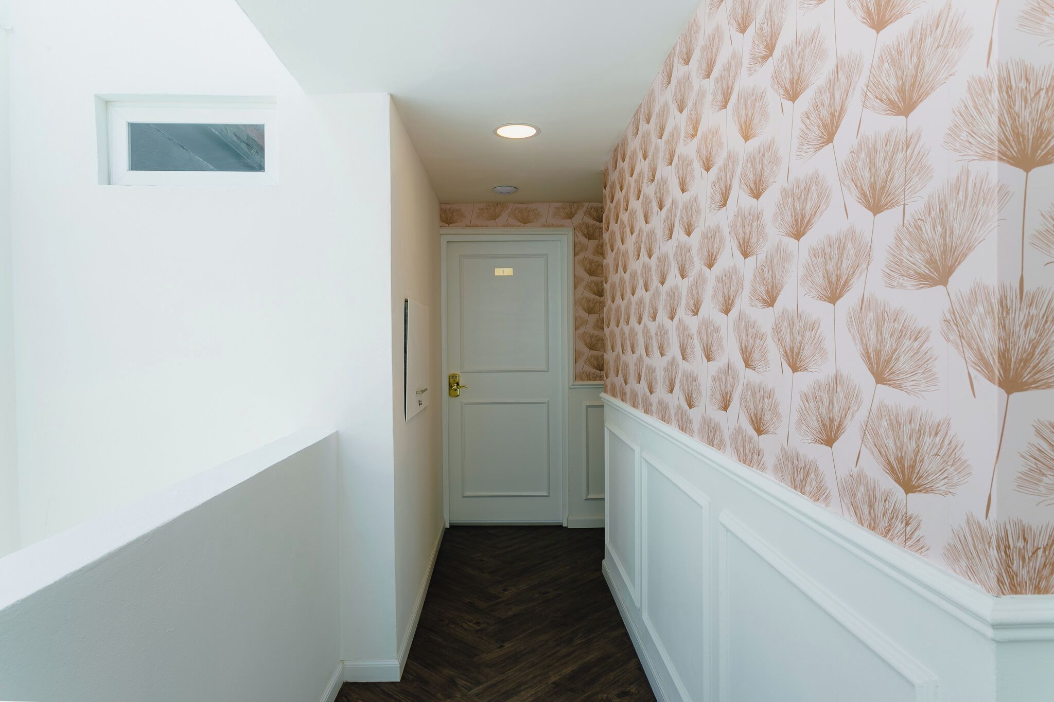 A hallway with a white door, a light switch, and a patterned wallpaper on the right wall.
