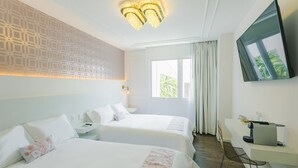 Habitación de hotel con dos camas, un escritorio con cafetera, televisión y ventana con cortinas.