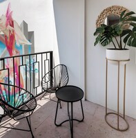 Un balcón con dos sillas negras, una planta en maceta y un espejo decorativo.