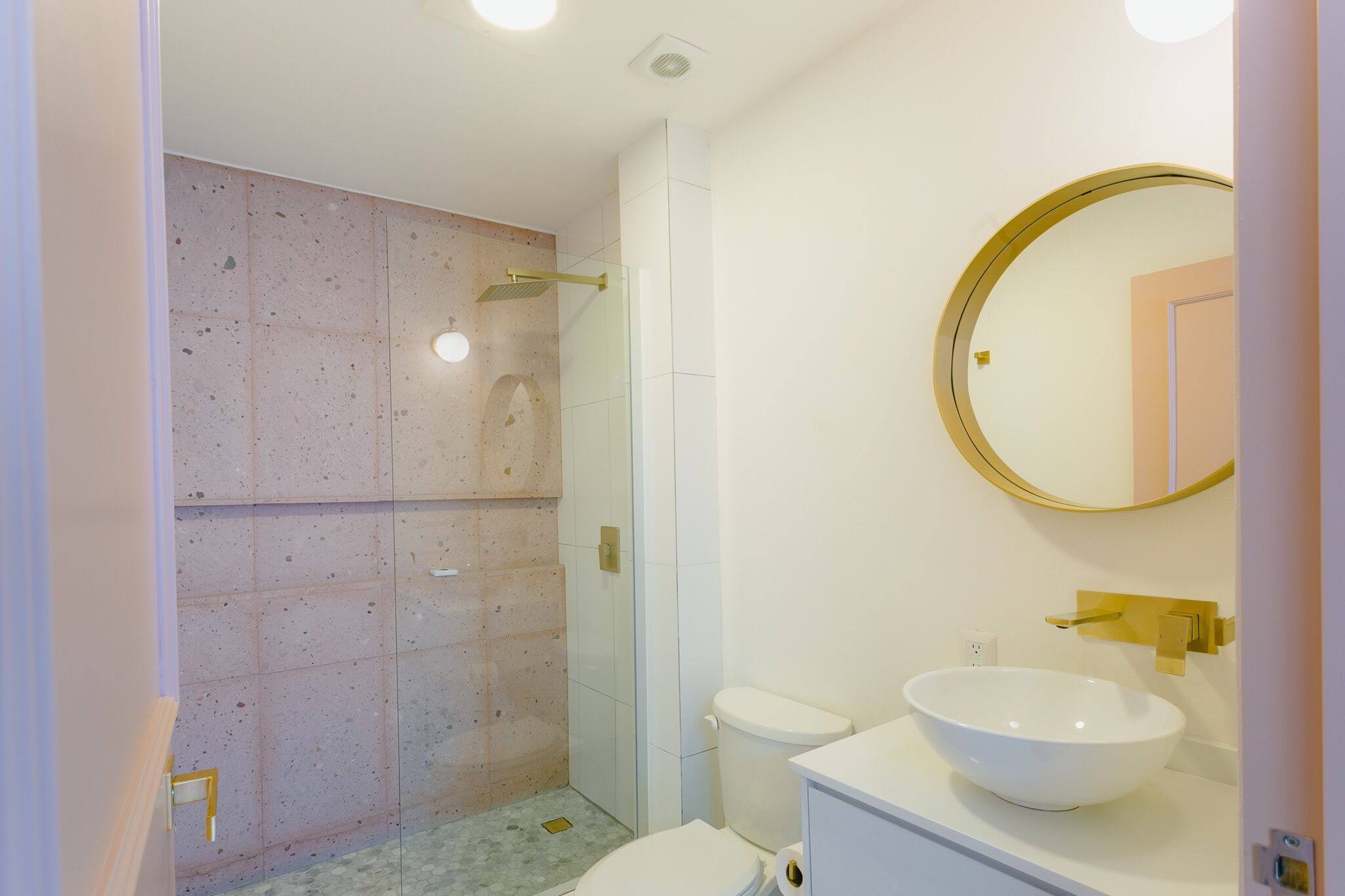 Un baño con ducha envuelta en vidrio, inodoro blanco y un lavamanos grande de color blanco con grifo dorado.