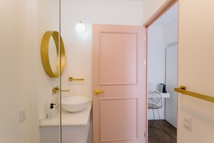 Un baño moderno con un lavamanos blanco, detalles dorados y una puerta rosa.