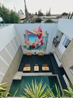 Un área de piscina en la azotea con un mural, asientos y vistas de la ciudad.