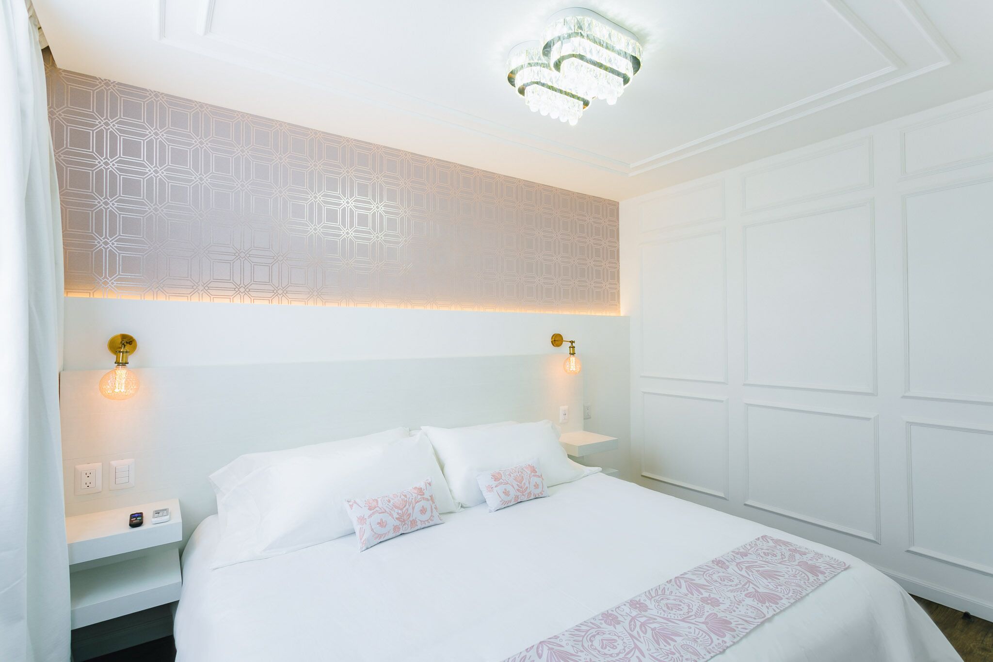 A hotel room with a large bed, two bedside tables, a wall with geometric patterns, and a chandelier.