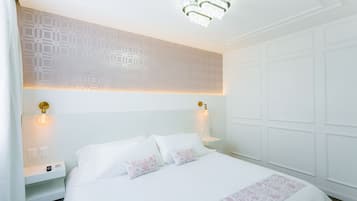 A hotel room with a large bed, two bedside tables, a wall with geometric patterns, and a chandelier.