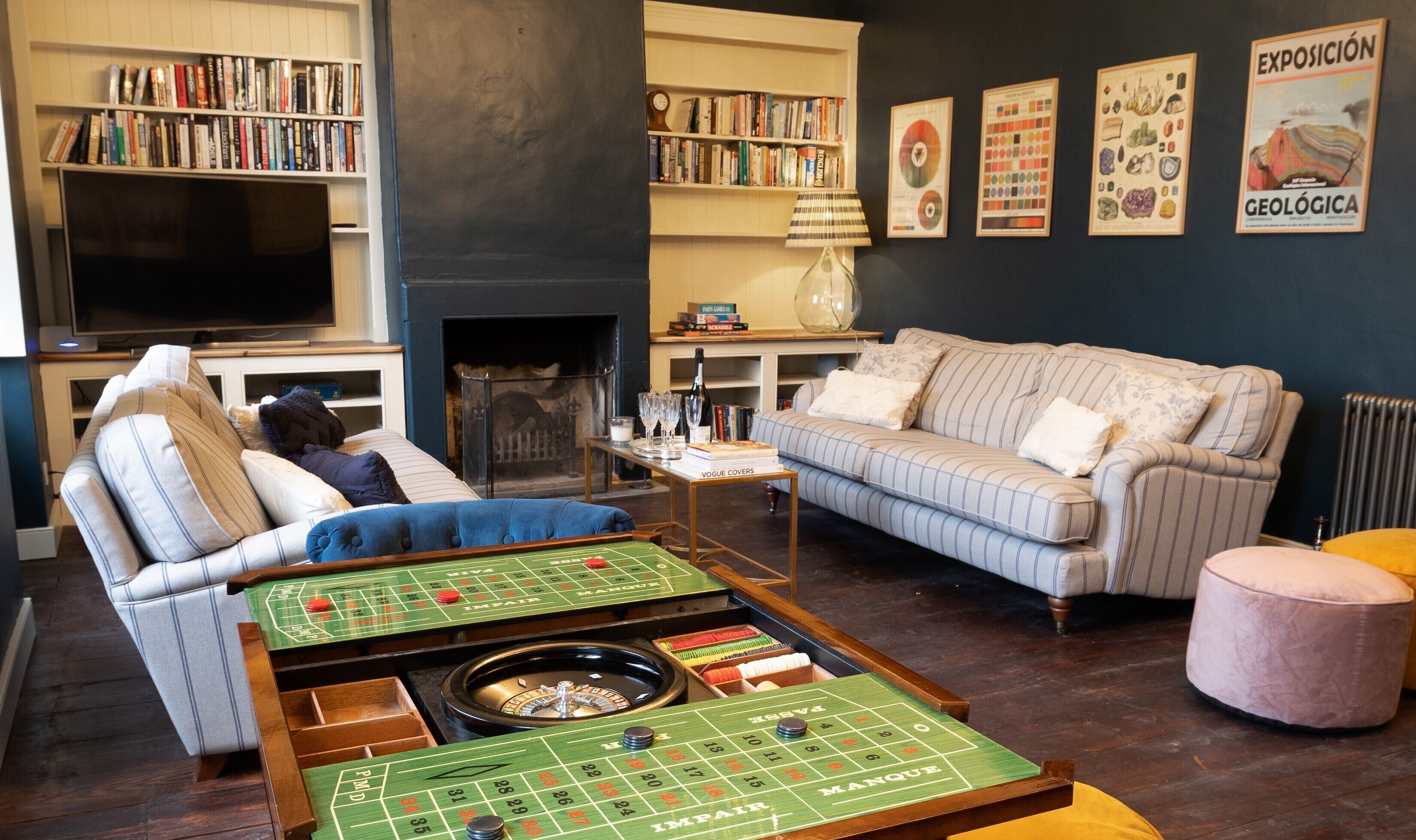 A cozy living room with striped sofas, a green craps table, and a bookshelf filled with books.