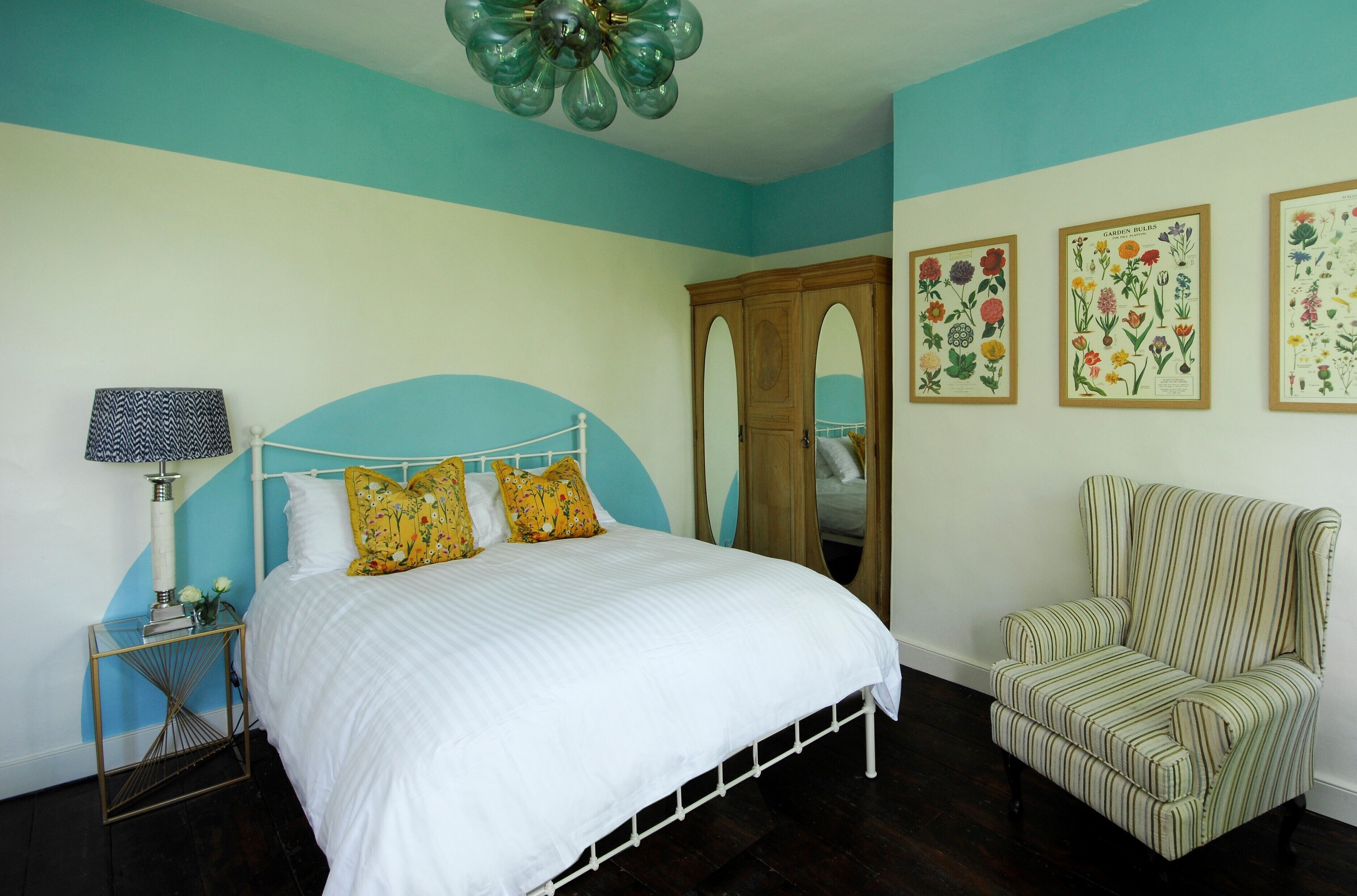 A bedroom with a bed, a chair, a nightstand, and wall art.