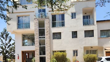 A multi-story residential building with a paved driveway and parked vehicles.