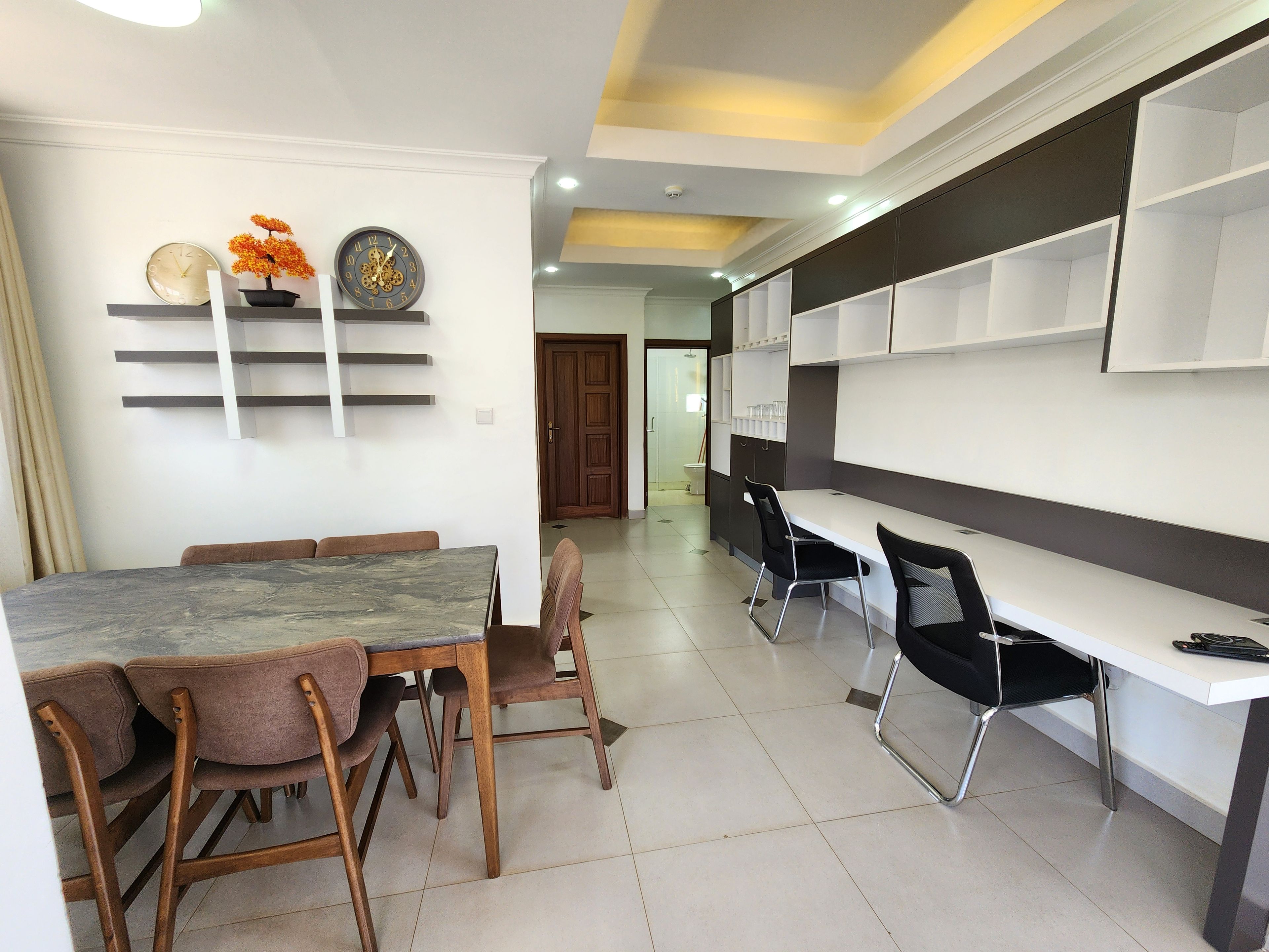 A modern dining area with a marble table, wooden chairs, and a white wall with shelves.