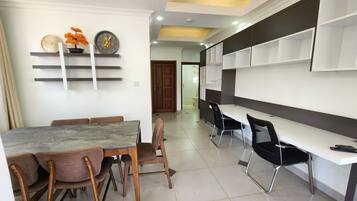 A modern dining area with a marble table, wooden chairs, and a white wall with shelves.