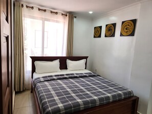 A neatly made bed with a checkered bedspread, a wooden headboard, and three wall-mounted artworks. - Red Rose Apartment, Unit # 401 (Kigali)
