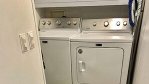 A laundry room with two stacked washers and dryers, a tiled floor, and a door with an electrical outlet.
