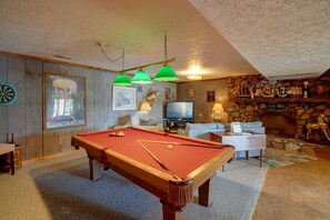 Ein Billardtisch in einem Raum mit Kamin, Fernseher und Dartscheibe.