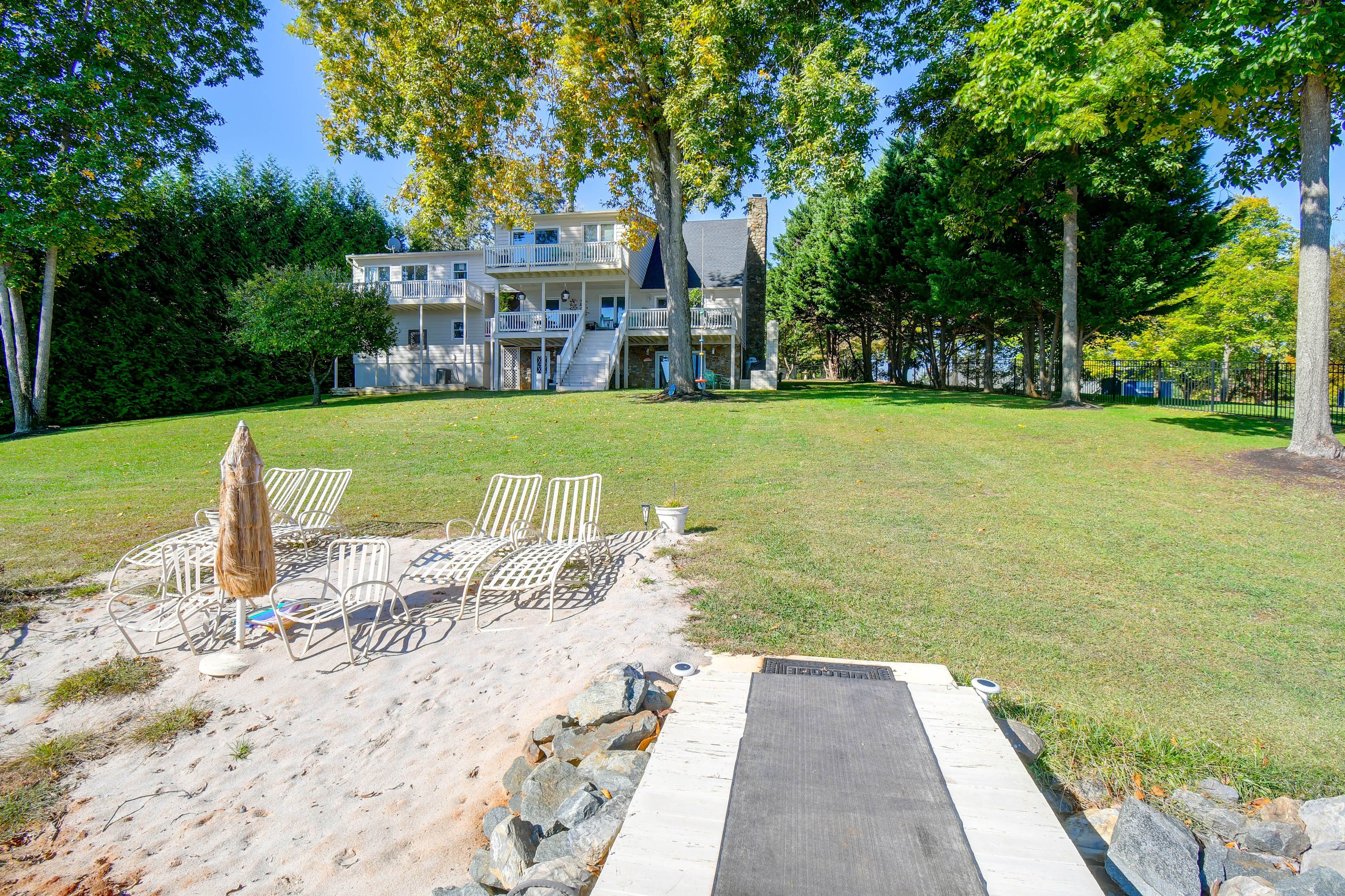 A two-story building with a stone facade, a grassy yard, and a paved area with chairs and a table.
