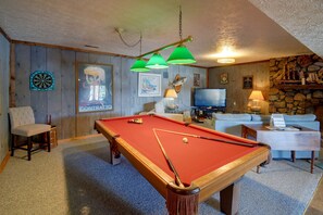 Ein Billardtisch mit roter Spielbahn, ein Fernseher und eine Sitzecke mit einer Couch und einem Sessel.