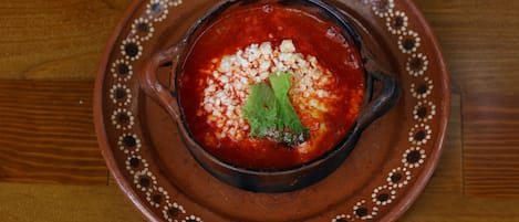 A bowl of red soup with a garnish on a patterned plate.
