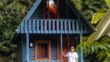 Una piccola casetta a un piano con veranda, immersa nel verde.