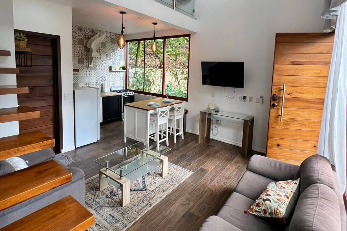 A modern living space with a staircase, a dining area, a kitchen, and a seating area with a sofa and a TV.