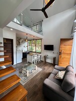 A modern living space with a staircase, a dining area, a kitchen, and a seating area with a sofa and a TV.