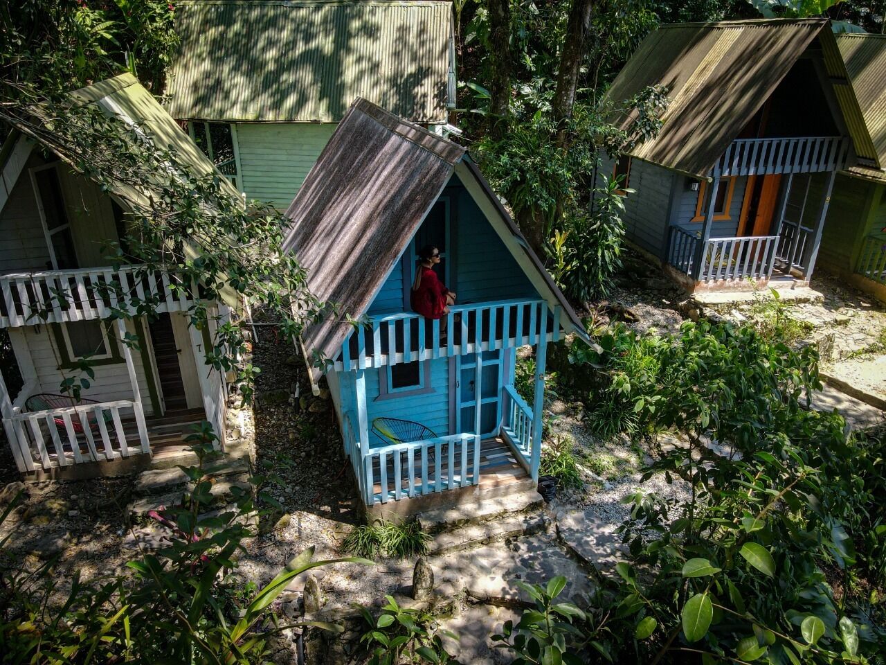 A small, rustic wooden house with a porch, surrounded by dense foliage.