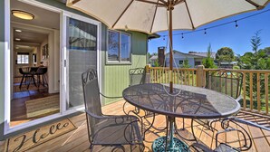 Une terrasse avec une table ronde et des chaises, un grand parasol et un paillasson sur lequel est écrit « Bonjour ».
