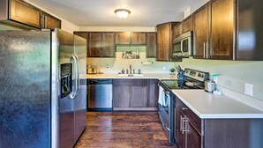 A modern kitchen with stainless steel appliances, wooden cabinets, and a white countertop.