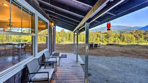 A covered outdoor seating area with tables and chairs, overlooking a natural landscape with trees and mountains.