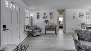 Een moderne woonkamer met een grijze bank, een fauteuil met een patroon, een kleine tafel met een plant en een eethoek op de achtergrond.