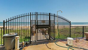 A gated area with a view of the beach, a metal gate, and a bench.