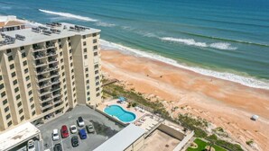A high-rise hotel with a rooftop pool, beach view, and parking area.