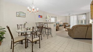 A dining area with a chandelier, a bar, and a living room with a sofa and a TV.