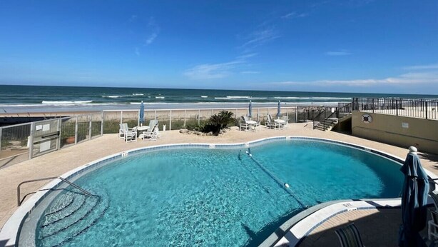 A swimming pool with a view of the ocean, surrounded by lounge chairs and a fence.