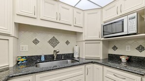 A kitchen with white cabinetry, a granite countertop, a microwave, and a sink.