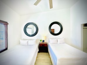 Une chambre d’hôtel avec deux lits simples, une table de chevet avec une lampe et deux miroirs fixés au mur.