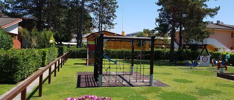 Un parque infantil con una estructura para escalar, un tobogán y una zona vallada.