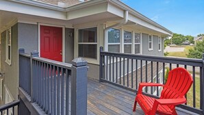 Une maison d’habitation avec une terrasse en bois, une porte rouge et un fauteuil Adirondack rouge.